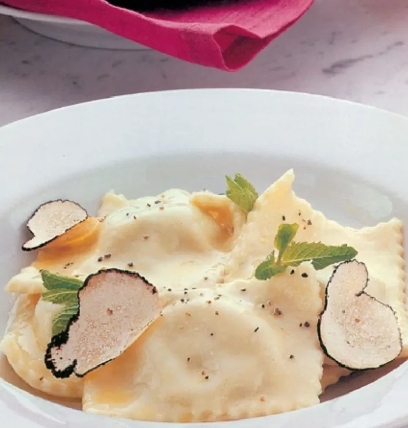 Agnolotti with ricotta and truffle on a white plate with truffle slices and mint leaves