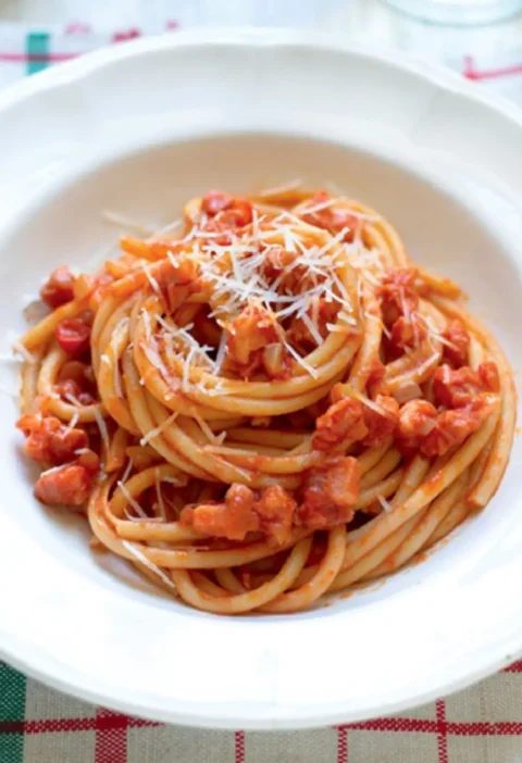 Amatrice-style bucatini with pancetta tomato sauce and grated pecorino in a white bowl