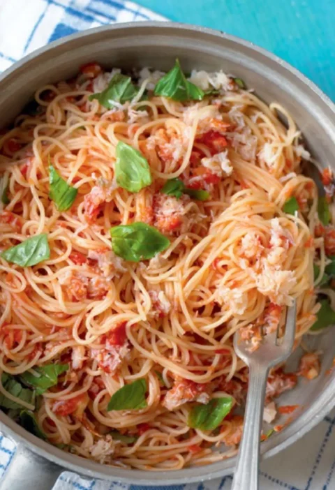 Angel's hair with crab in a pan with tomato sauce, crab meat and fresh basil leaves, a fork resting in the pasta