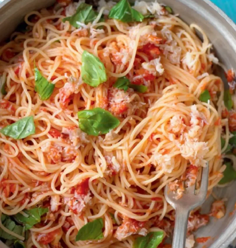 Angel's hair with crab in a pan with tomato sauce, crab meat and fresh basil leaves, a fork resting in the pasta