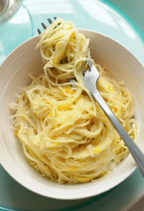 Angel's hair with lemon twirled on a fork above a white bowl of pasta with lemon zest and Parmesan
