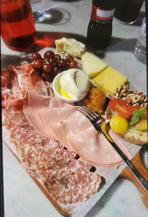 Antipasto board with mortadella, salami, prosciutto, mozzarella, cheeses, grapes, walnuts and tomato toasts