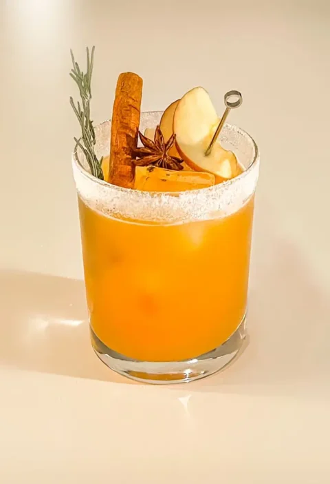 Apple cider margarita in a sugar-rimmed glass with apple slices, cinnamon stick, star anise and rosemary