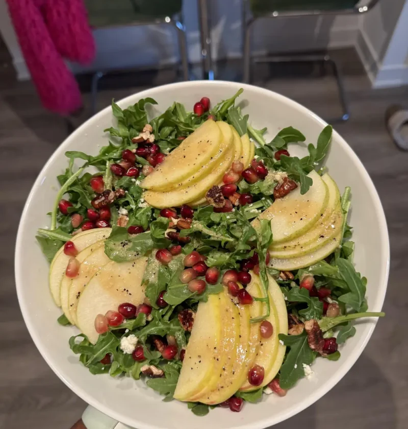 Arugula pear parmesan salad in a white bowl with fruit slices, pomegranate seeds and pecans