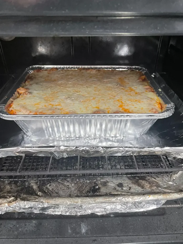 Baked Ziti with Red Sauce covered in melted cheese baking in the oven in a foil pan