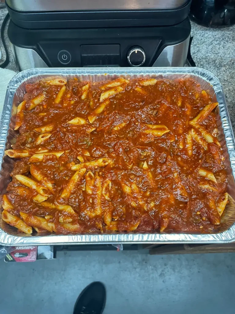 Penne pasta coated in thick meat sauce in a foil pan before the cheese layer is added