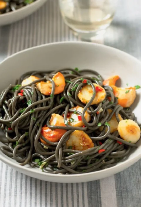 Black Angel's Hair with Scallops in a white bowl with seared scallops, red chili and parsley