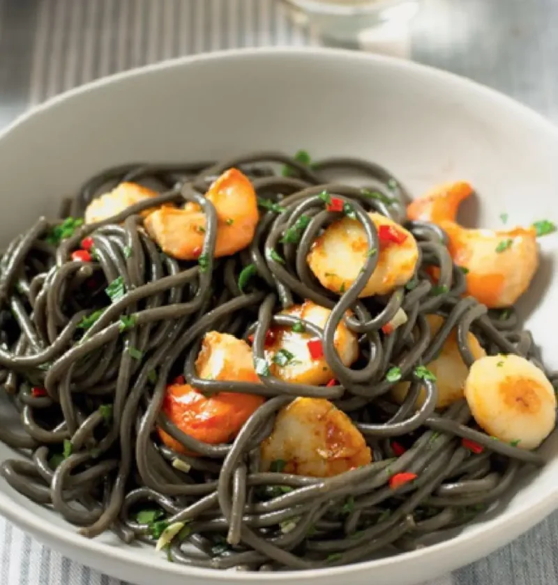 Black Angel's Hair with Scallops in a white bowl with seared scallops, red chili and parsley