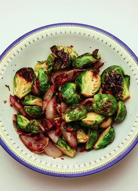Roasted Brussels sprouts with pancetta and red onion in a white bowl with a blue rim