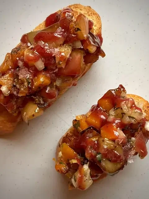 Two butternut squash crostini topped with roasted squash, tomato and balsamic dressing on a white plate