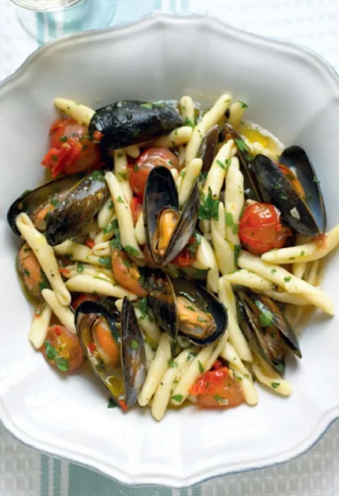 Cavatelli with mussels and cherry tomatoes in a white bowl, sprinkled with chopped parsley