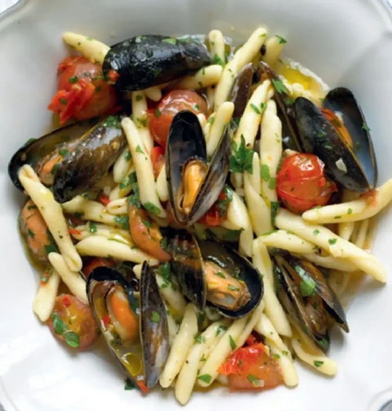 Cavatelli with mussels and cherry tomatoes in a white bowl, sprinkled with chopped parsley