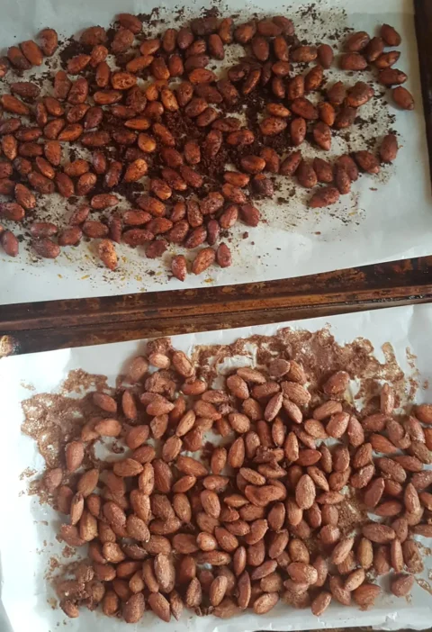 Cinnamon and vanilla glazed roasted almonds spread on two parchment-lined baking sheets