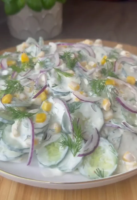 Creamy cucumber salad with red onion, corn and fresh dill on a white plate