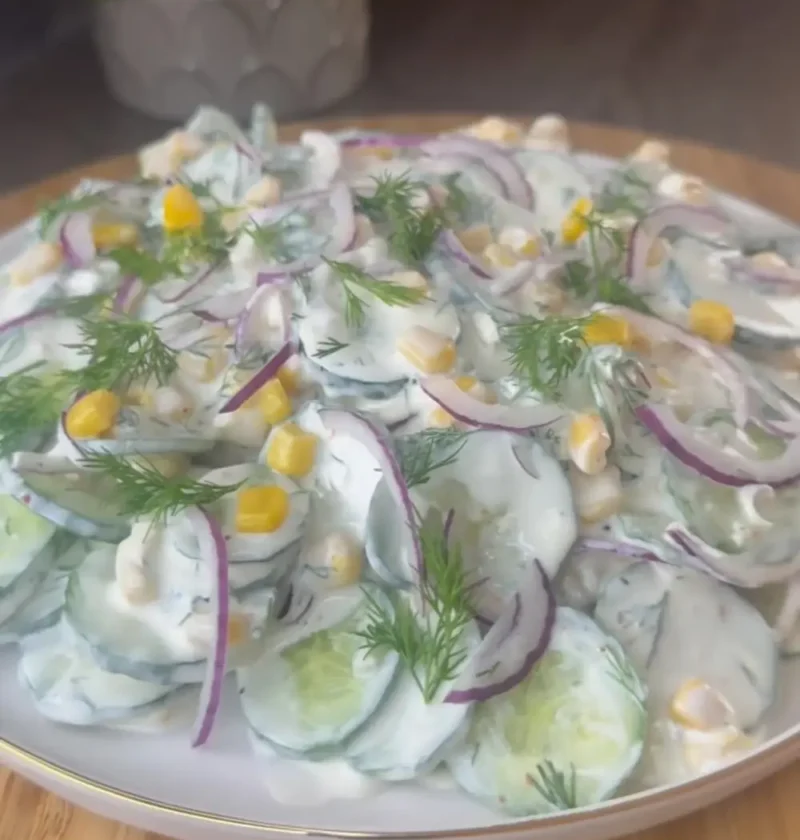 Creamy cucumber salad with red onion, corn and fresh dill on a white plate