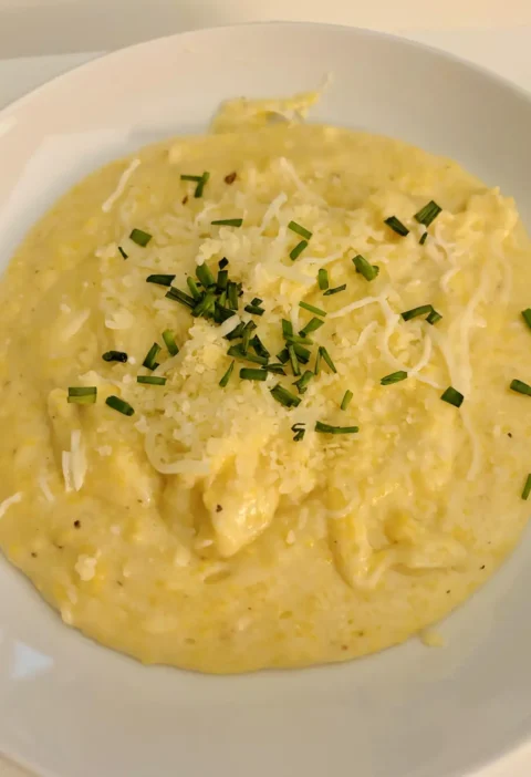 Creamy polenta in a white bowl topped with grated Parmesan and chopped chives