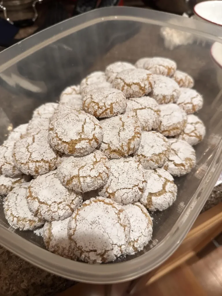Easy amaretti cookies with crackled powdered sugar tops piled in a plastic container