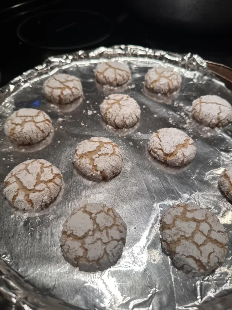 Baked amaretti cookies with cracked tops cooling on a foil lined pan