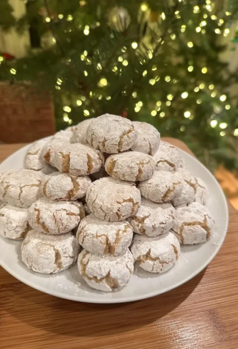 Easy amaretti cookies stacked on a white plate with a Christmas tree behind