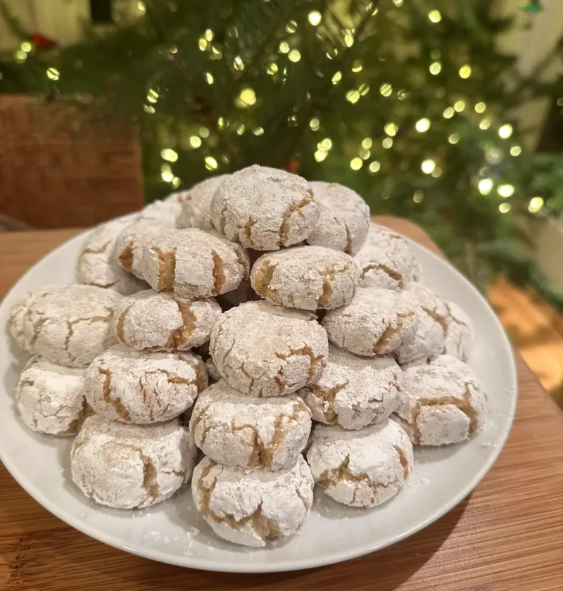 Easy amaretti cookies stacked on a white plate with a Christmas tree behind