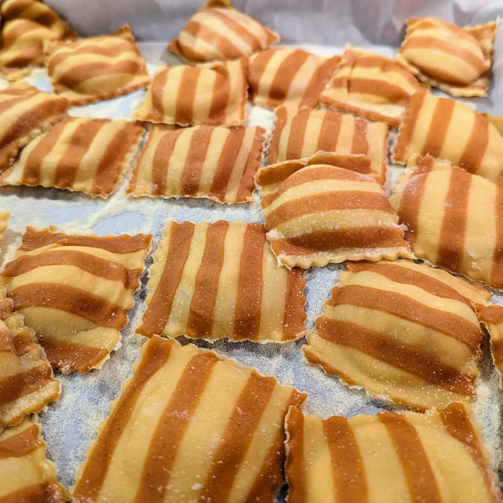Uncooked striped orange and cream butternut squash ravioli drying on a tray dusted with semolina