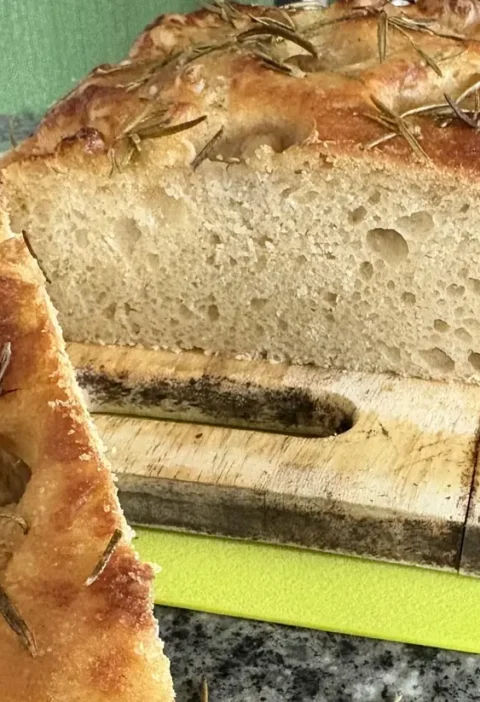 Golden easy focaccia with grapes and rosemary sliced open to show the airy holes inside