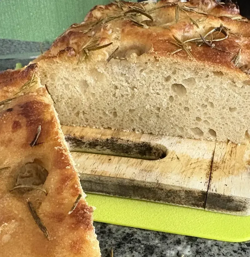 Golden easy focaccia with grapes and rosemary sliced open to show the airy holes inside