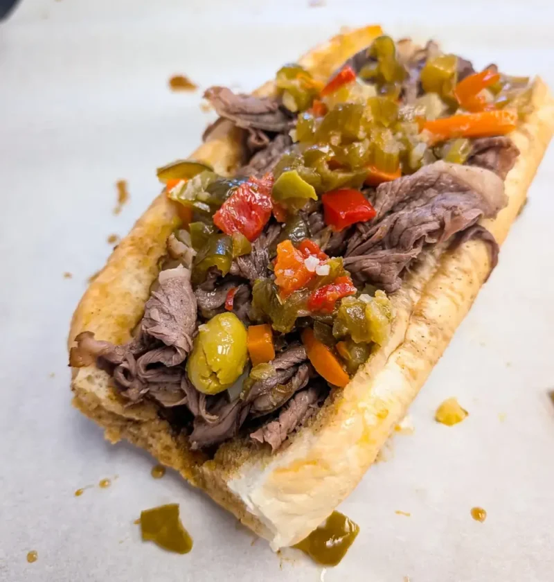 Italian beef sandwich in a toasted roll topped with sliced beef and giardiniera peppers and olives
