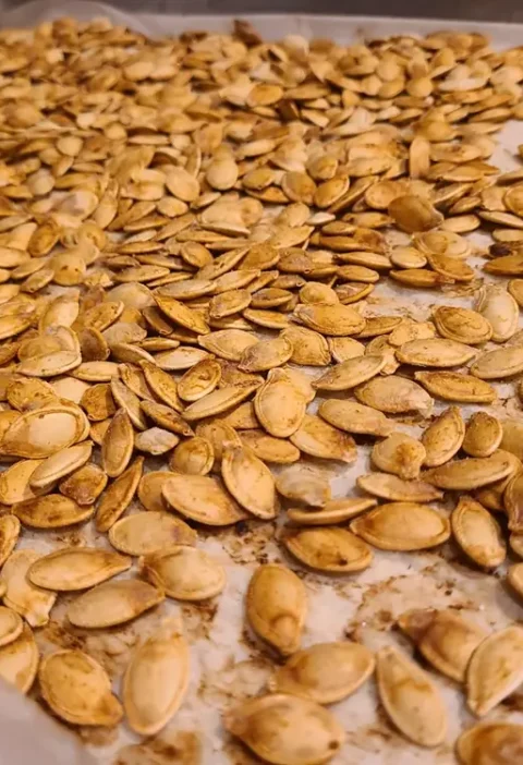 Roasted golden Italian pumpkin seeds spread on a parchment-lined baking sheet