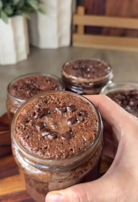 A hand holding a jar of no-bake chocolate cake topped with chocolate chips, with more jars behind