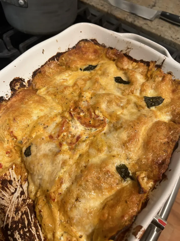 Baked pumpkin lasagna in a white dish with browned cheese and crisp sage leaves on top