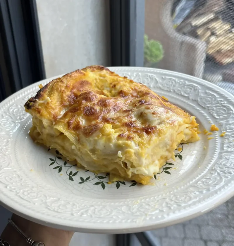 A square slice of easy pumpkin lasagna with golden layers and browned cheese on a white plate