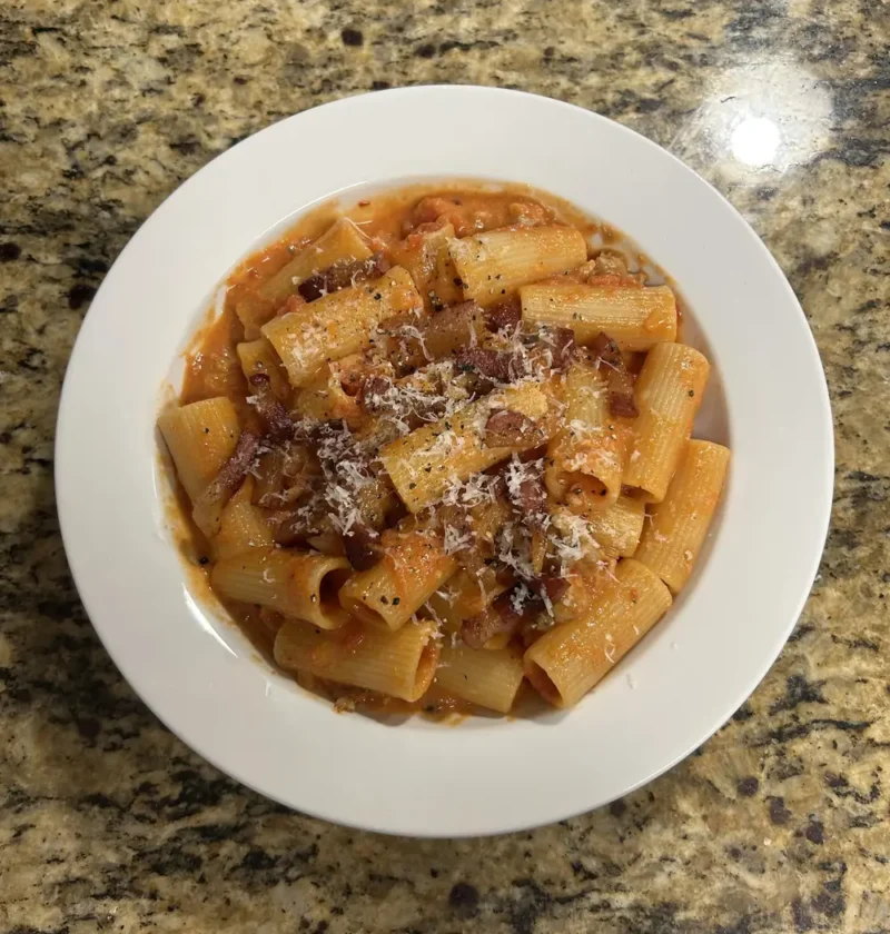 Rigatoni alla zozzona topped with crisp guanciale and grated pecorino in a white bowl