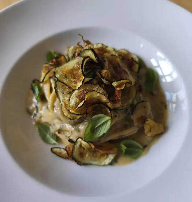 Spaghetti alla Nerano in a white bowl topped with crispy fried zucchini slices and fresh basil leaves