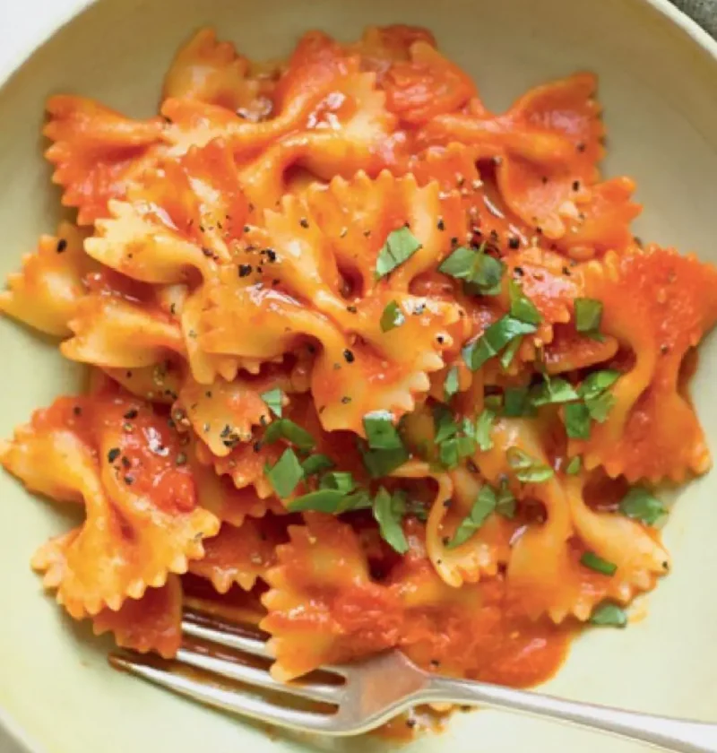 Bowl of farfalle Genoese-style in a smooth tomato sauce topped with chopped basil and a fork