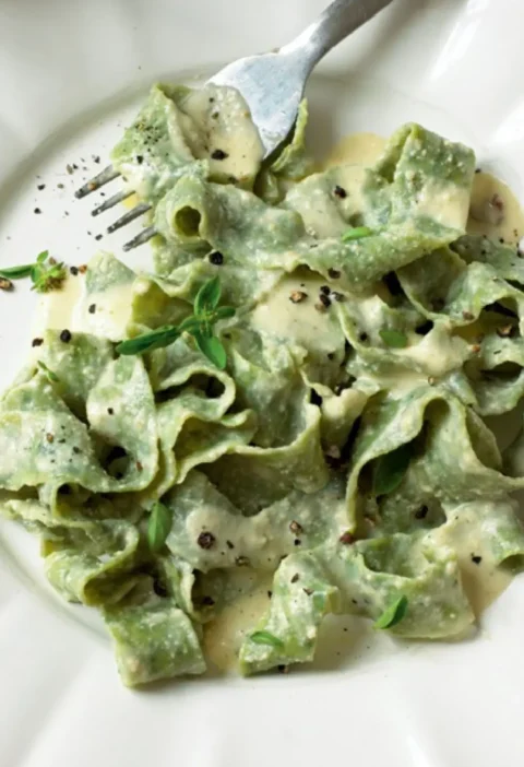 Fettuccine verdi with walnut sauce on a white plate with black pepper and marjoram leaves