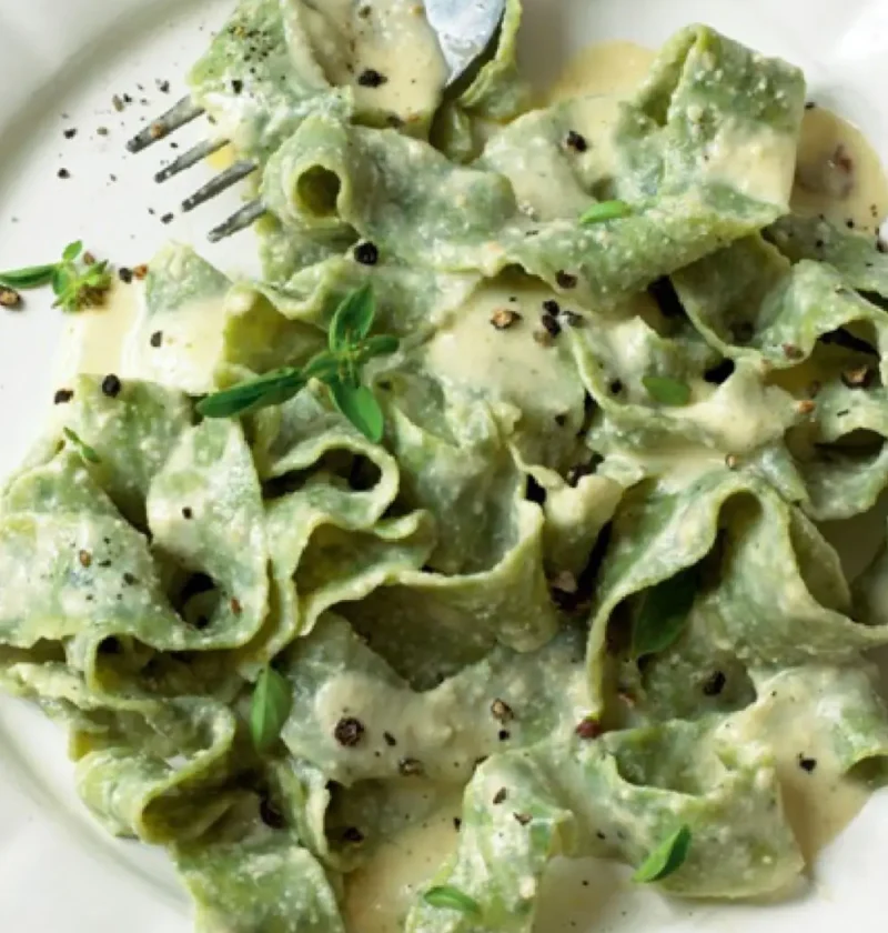 Fettuccine verdi with walnut sauce on a white plate with black pepper and marjoram leaves