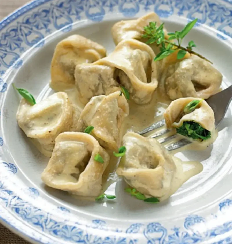 Filled pasta with walnut sauce in a blue and white bowl, one piece cut open on a fork to show the green filling