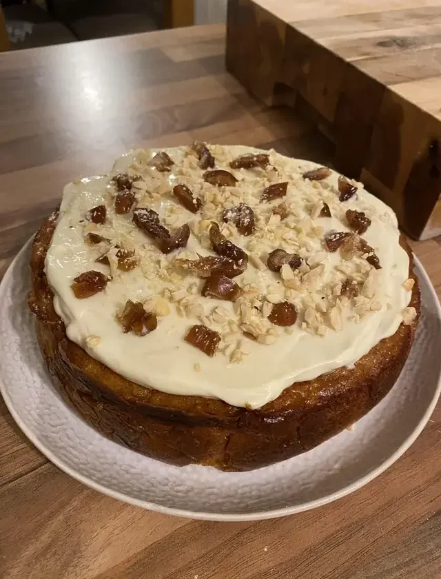 Flourless almond pumpkin torta with cream cheese frosting, chopped almonds and dates on a white plate