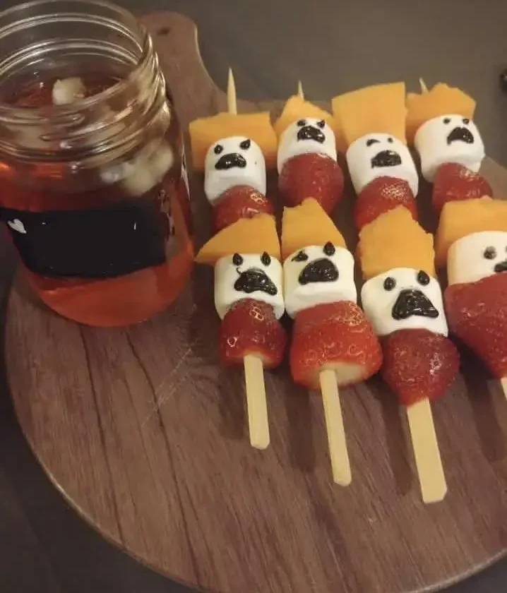 Halloween ghost fruit skewers with strawberries, marshmallow ghosts and cantaloupe on a wooden board next to a jar of punch