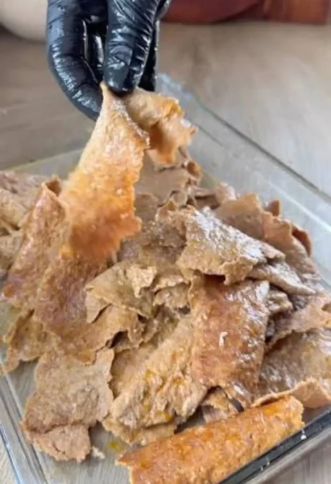 Shredded crisp homemade doner kebab meat being lifted from a glass baking dish