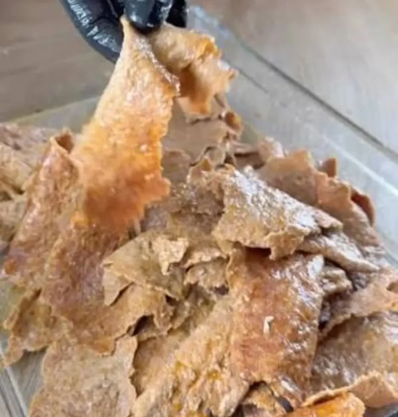 Shredded crisp homemade doner kebab meat being lifted from a glass baking dish