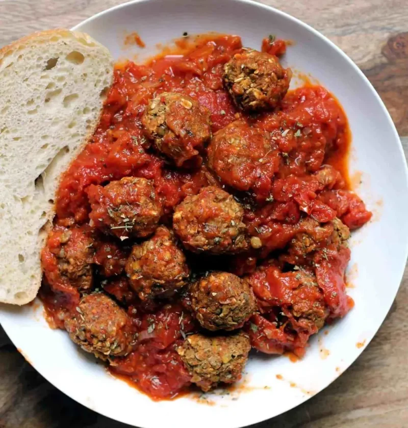 Italian meatballs with simple tomato sauce in a white bowl with a slice of crusty bread
