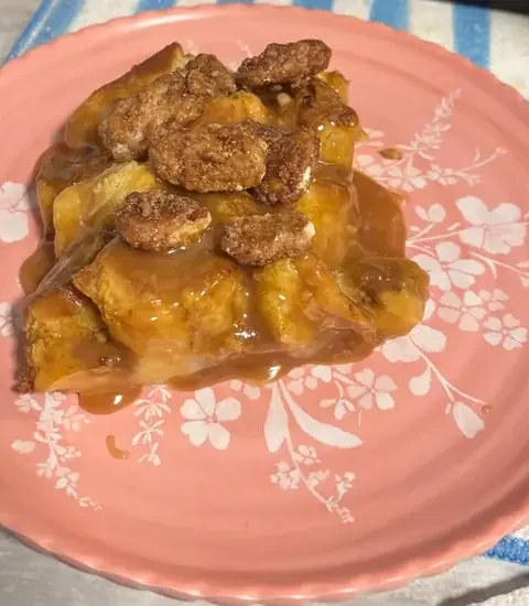 Italian panettone pumpkin bread pudding topped with candied pecans and caramel sauce on a pink floral plate