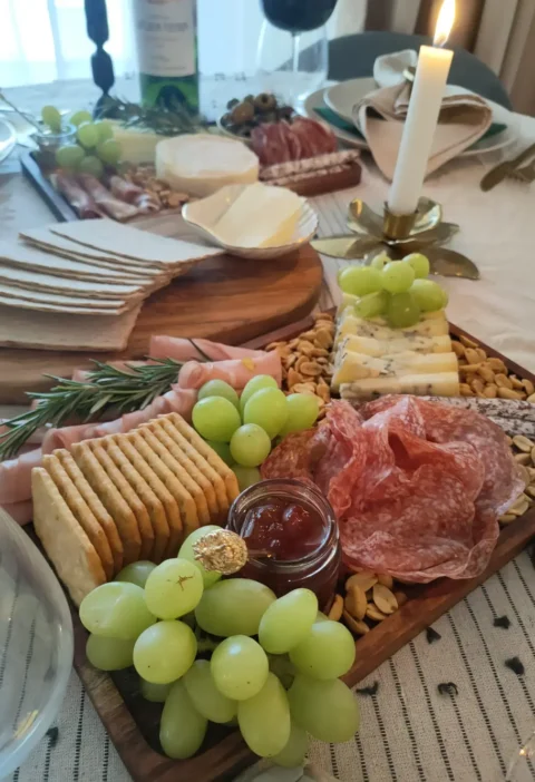 Italian party platter with salami, cheeses, crackers, green grapes, nuts, jam and rosemary on wooden boards