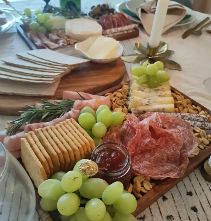 Italian party platter with salami, cheeses, crackers, green grapes, nuts, jam and rosemary on wooden boards