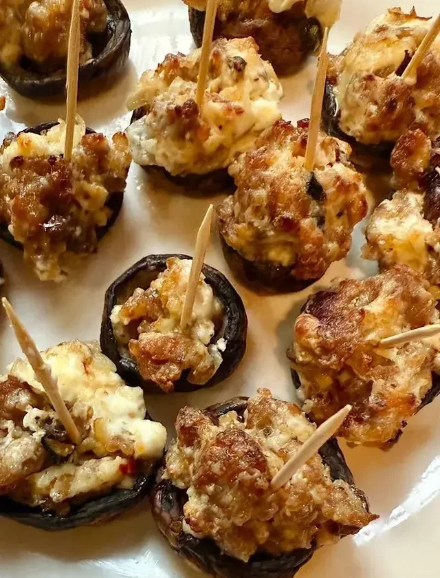 Baked Italian stuffed mushrooms topped with browned sausage and melted cheese, each with a toothpick, on a white plate