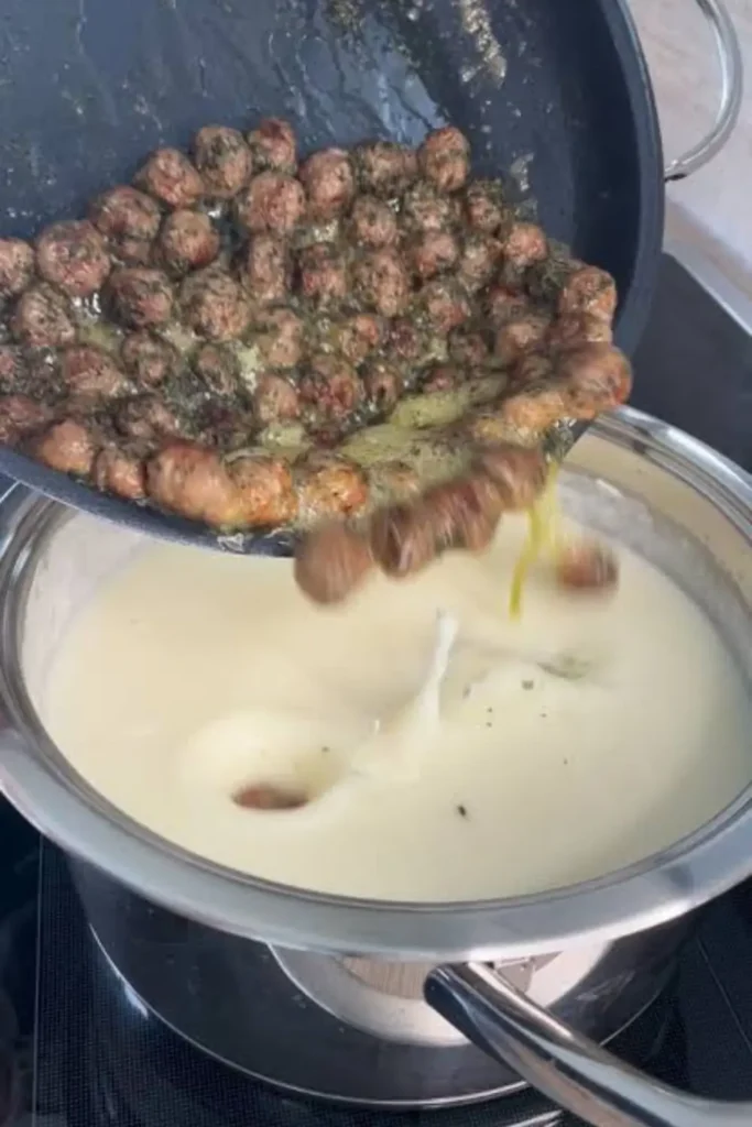 Browned mini meatballs with mint butter being poured into a pot of creamy yogurt soup for Lebeniye soup