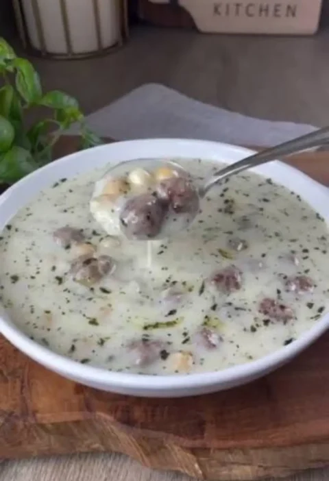Spoonful of Lebeniye soup with meatballs and chickpeas over a white bowl of creamy yogurt soup flecked with mint