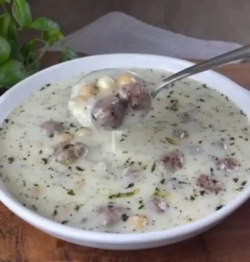 Spoonful of Lebeniye soup with meatballs and chickpeas over a white bowl of creamy yogurt soup flecked with mint